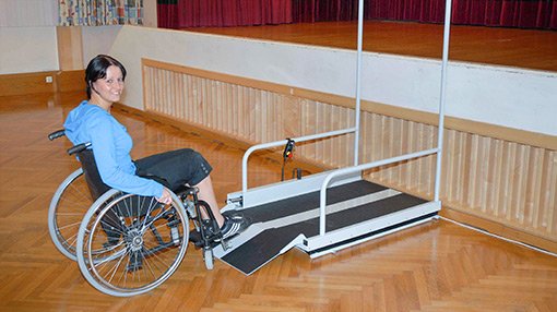 Eine junge Dame benutzt mit ihrem Rollstuhl den LIFTBOY, um die Bühne zu erreichen