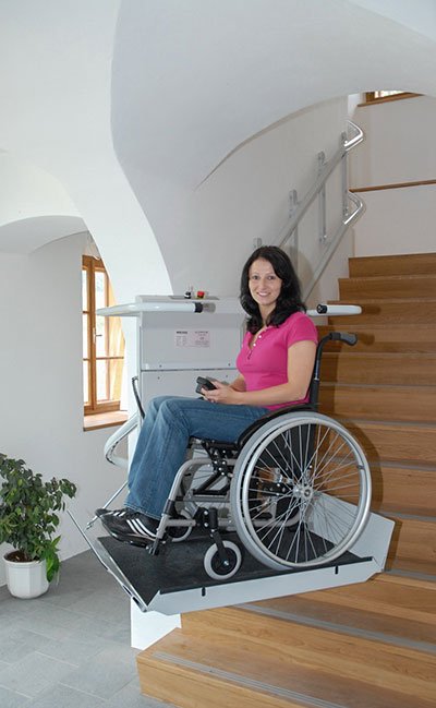 Eine junge Dame benutzt mit ihrem Rollstuhl den Plattformtreppenlift OMEGA im Innenbereich